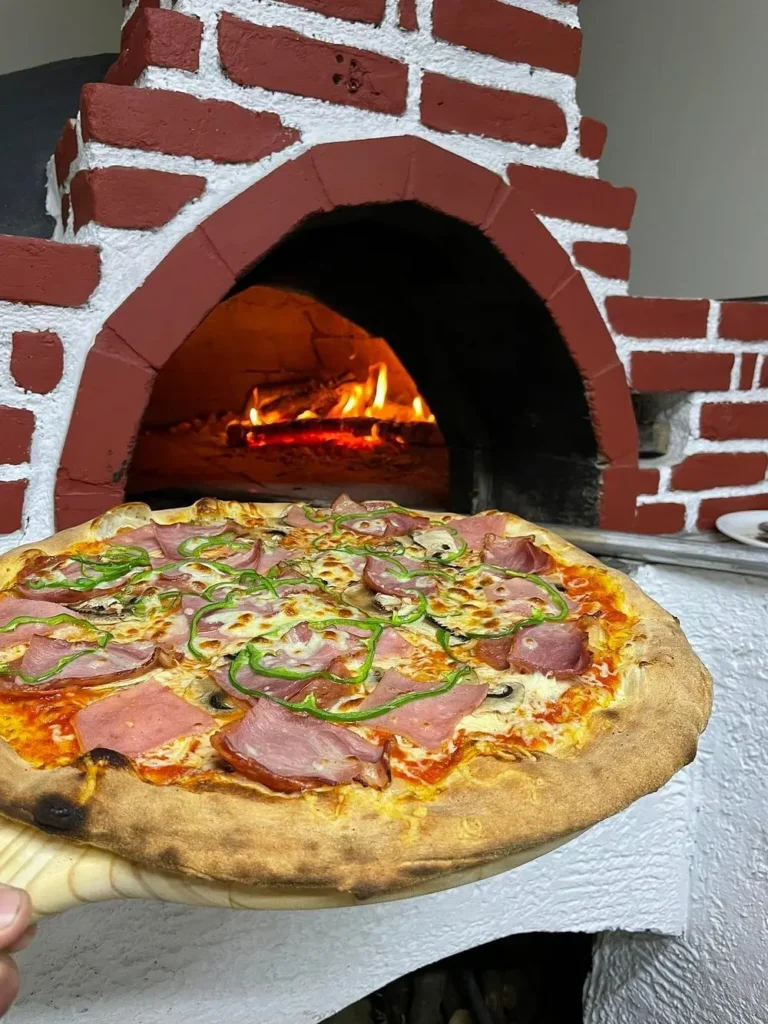 Freshly prepared pizza on a wooden peel about to enter a traditional wood-fired brick oven at Oregano’s in Chania.